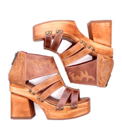 Two Orphyx platform sandals by Bed|Stü in brown leather, featuring sculpted wood platforms, decorative stitching, metal rivets, and layered leather straps in an open-toe silhouette, positioned side by side on a white background.