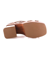 The image shows the bottom view of the Bed|Stü Orphyx brown heeled sandal, featuring a smooth sole, layered leather straps, and a square-shaped heel.
