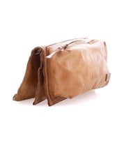 The Bed|Stü Parle is a light brown soft leather bag with two zippered compartments and a zipper closure, shown against a white background. The pouch has a slightly worn, flexible appearance.