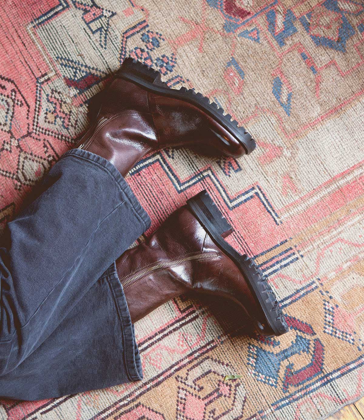 A person wearing dark pants and the Bed|Stü Ploy stylish Italian leather boots with dual side zippers is lying on a patterned, multicolored rug.