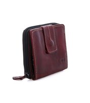 The Bed|Stü Plus is a dark brown bifold wallet with white stitching, featuring a zipper closure along the side and a snap button flap on the front. It includes a convenient zippered coin pocket and is photographed on a white background.