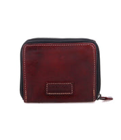 A small, rectangular, brown leather wallet by Bed|Stü called "Plus," featuring visible stitching, a stitched label on the front, and a convenient zippered coin pocket.