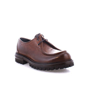 The Bed|Stü Portare is a brown leather moc-toe lace-up boot featuring a thick, rugged black sole, shown here against a white background.