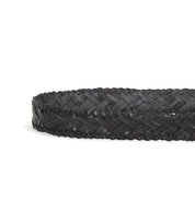 The Bed|Stü Proem belt, a black handwoven leather accessory with artisan detailing, is coiled on a white background.