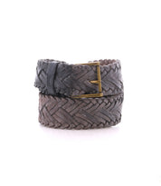 A handwoven leather belt by Bed|Stü, the Proem, showcases artisan detailing and a vintage metal buckle, rolled up and displayed against a white background.