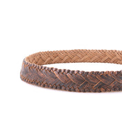 A close-up view of the Bed|Stü Proem handwoven brown leather belt, showcasing artisan detailing and a vintage metal buckle against a white background.