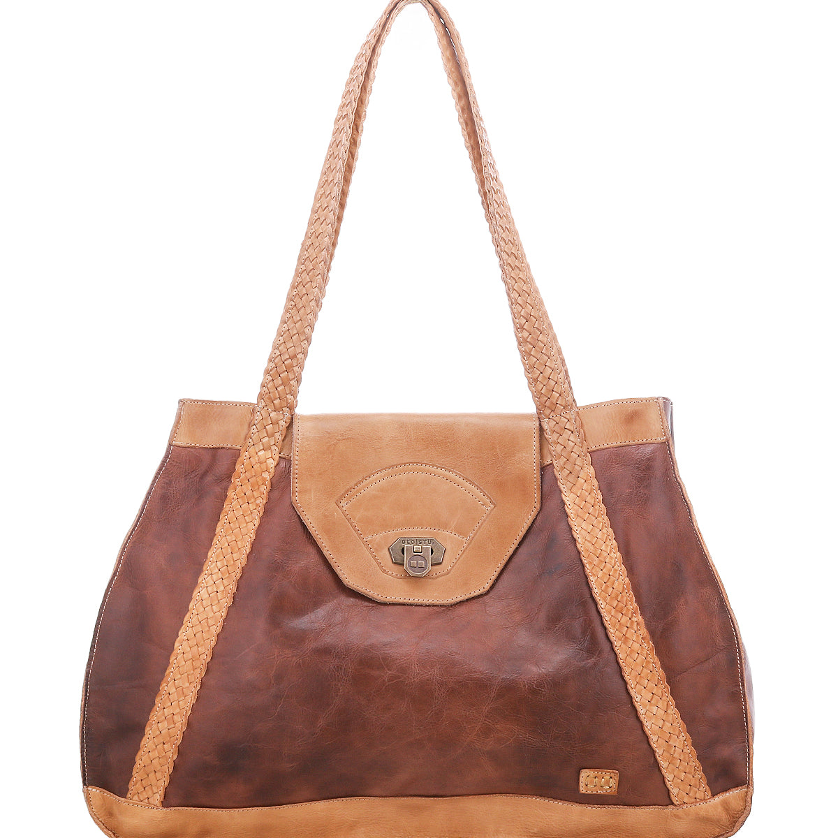 The Bed|Stü Proper is a two-tone brown leather tote with handwoven shoulder straps, flap closure, and a small metal logo plate on the lower right corner.