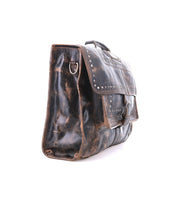 The Bed|Stü Pub is a distressed black leather messenger bag featuring metal studs, a front flap with buckle closure, and a side D-ring, shown against a white background—this stylish travel bag seamlessly blends the practicality of a work bag with the sleek sophistication of a modern leather briefcase.