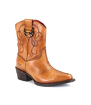 The Bed|Stü Rangeley is a tan leather cowboy boot adorned with decorative stitching and lines, featuring a side pull strap, low angled heel, and pointed toe for a distinctive look, shown against a white background.