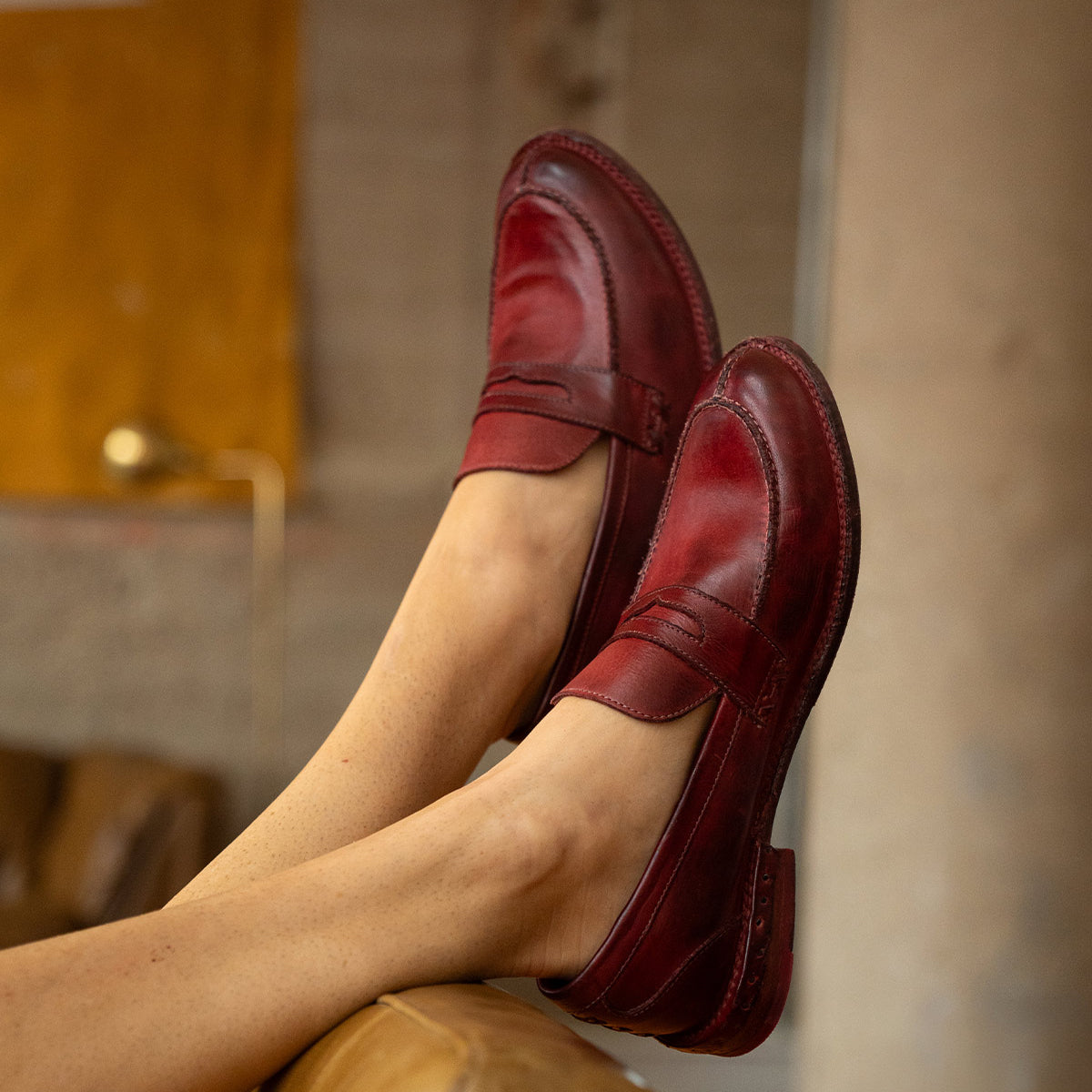 Deep red leather Reina penny loafers by Bed|Stü with a Goodyear welted construction worn on feet propped up on a chair.