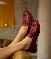 Deep red leather Reina penny loafers by Bed|Stü with a Goodyear welted construction worn on feet propped up on a chair.