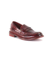 A single Reina penny loafer by Bed|Stü in maroon leather is displayed against a plain white background. This timeless design features a smooth leather upper, visible stitching, a low heel, and a slightly worn sole. Classic Goodyear welted construction combines durability with style.