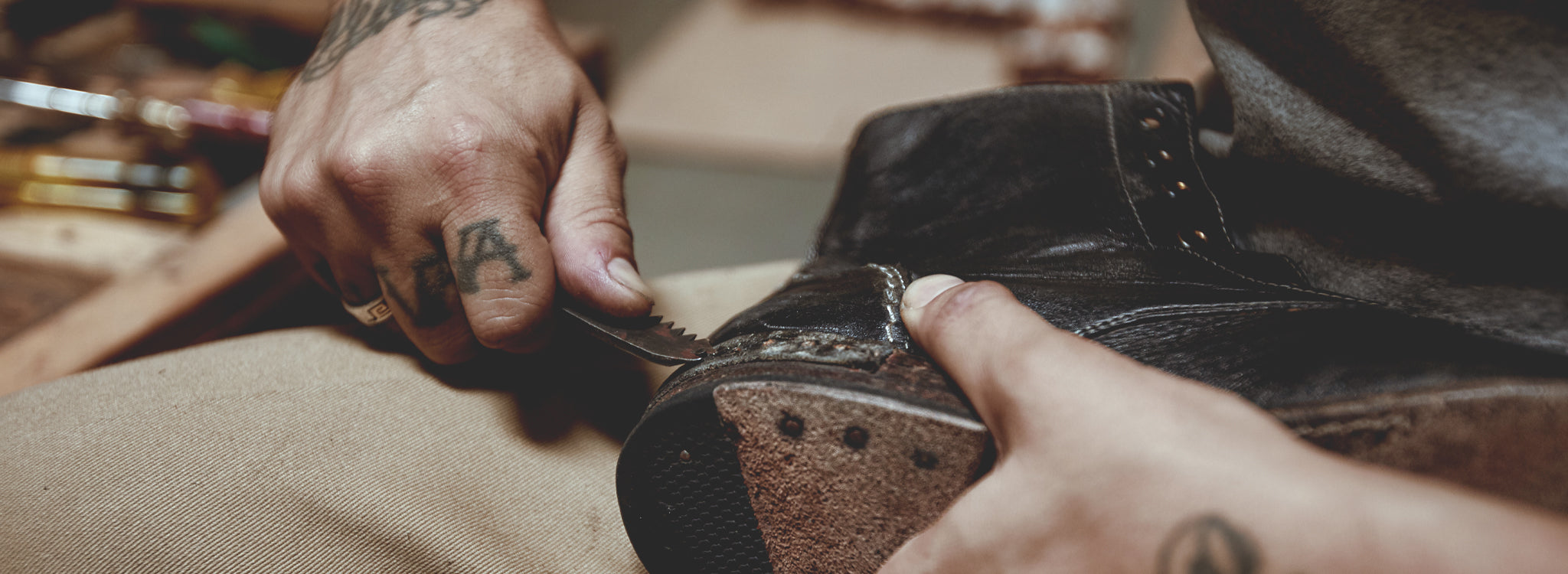 Hands repairing a black leather boot with a small tool along the sole.