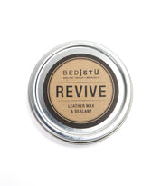 A round metal tin labeled "Bed|Stü Revive Leather Wax/Sealant" features a brown and black design on the lid, offering an ideal leather care solution with its natural wax-based formula.
