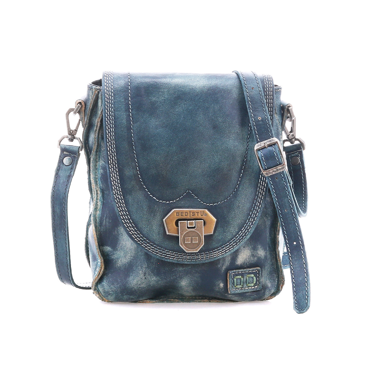 The Bed|Stü Rhyme is a small blue leather crossbody bag featuring a flap closure with metal clasp, adjustable strap, and visible stitching for added detail, offering hands-free convenience and shown against a white background.