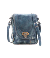 The Bed|Stü Rhyme is a small blue leather crossbody bag featuring a flap closure with metal clasp, adjustable strap, and visible stitching for added detail, offering hands-free convenience and shown against a white background.