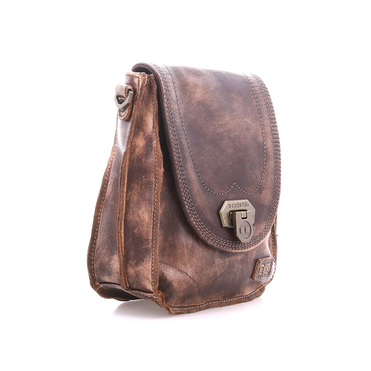 The Bed|Stü Rhyme crossbody bag, crafted in brown leather with a front flap, buckle closure, and visible stitching for a hands-free experience, is photographed on a white background.