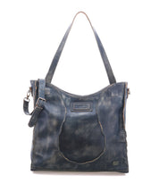 The Ridgefield by Bed|Stü is a dark blue full-grain leather tote bag with a distressed finish, main shoulder strap, side buckle detail, and visible seams. It features an organized interior—making it the perfect daily tote—and is displayed against a plain white background.