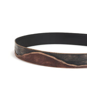 The Bed|Stü Riven is a black leather belt featuring a brown, distressed, wavy pattern along the lower edge. Shown looped against a white background, it’s an ideal everyday accessory that combines durability with classic style.