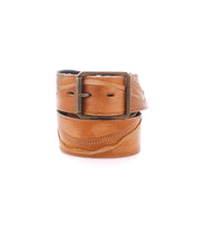 Introducing the Riven by Bed|Stü: a sturdy tan leather belt featuring a brass buckle, artfully rolled and photographed on a white background—ideal for everyday wear.