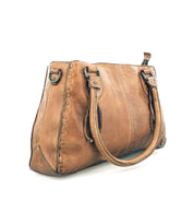 The Bed|Stü Rockababy is a brown compact leather bag with dual handles, decorative stitching along the sides, and a visible zipper, shown on a white background. Expertly crafted from premium vegetable-tanned leather, this handbag blends timeless style with exceptional durability.