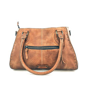 Introducing the Rockababy by Bed|Stü—a compact brown leather handbag crafted from vegetable-tanned leather. It features two handles, a visible front zipper pocket, and distinctive stitched detailing. The bag is showcased against a plain white background.