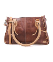 The Bed|Stü Rockababy is a compact brown leather handbag crafted from vegetable-tanned leather, featuring light tan handles and stitching, metal hardware, and a rectangular shape. The bag is photographed on a white background.
