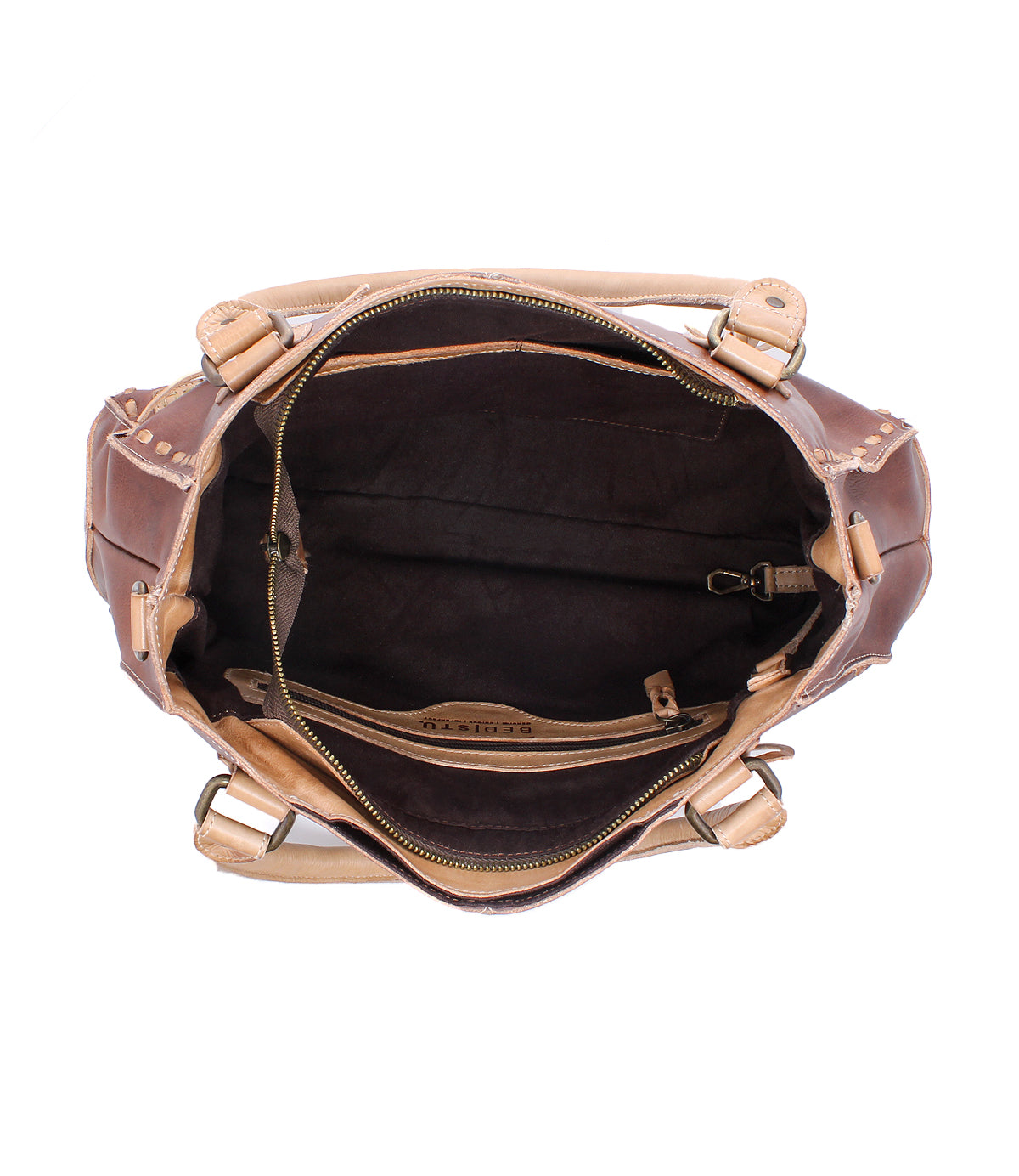 The Bed|Stü Rockababy is an open brown and beige vegetable-tanned leather handbag, featuring a spacious main compartment, interior zip pocket, key clip, and dark fabric lining as seen from above. It includes a crossbody strap for versatile carrying options.