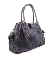 The Bed|Stü Rockaway is a large black full-grain leather handbag featuring two handles, a shoulder strap, and visible stitching with a distressed, worn texture. Photographed on a white background, this bag is designed for everyday function, combining durability with timeless style.