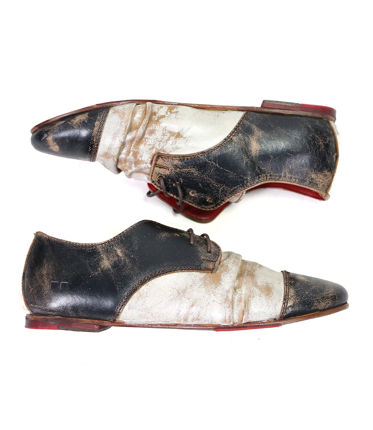 Step out in style with the Bed|Stü Rumba II — a pair of two-tone lace-up leather shoes featuring striking black and white panels, distinctive red soles, and intentional distressing for a vintage-inspired charm. Shown in side view facing opposite directions, these shoes effortlessly blend comfort and timeless appeal.