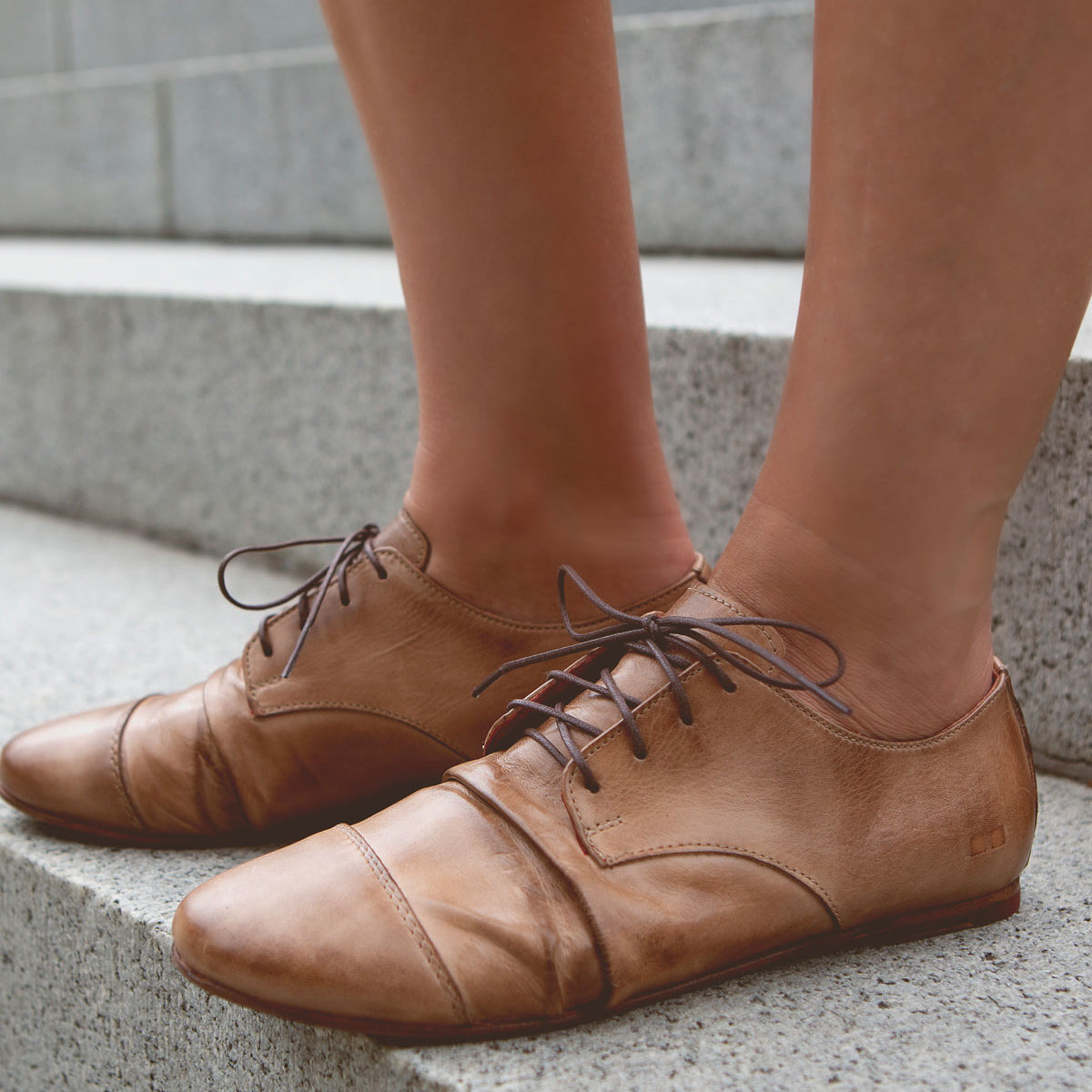 A person wearing the Bed|Stü Rumba II stylish comfort brown lace-up leather shoes stands on concrete steps.
