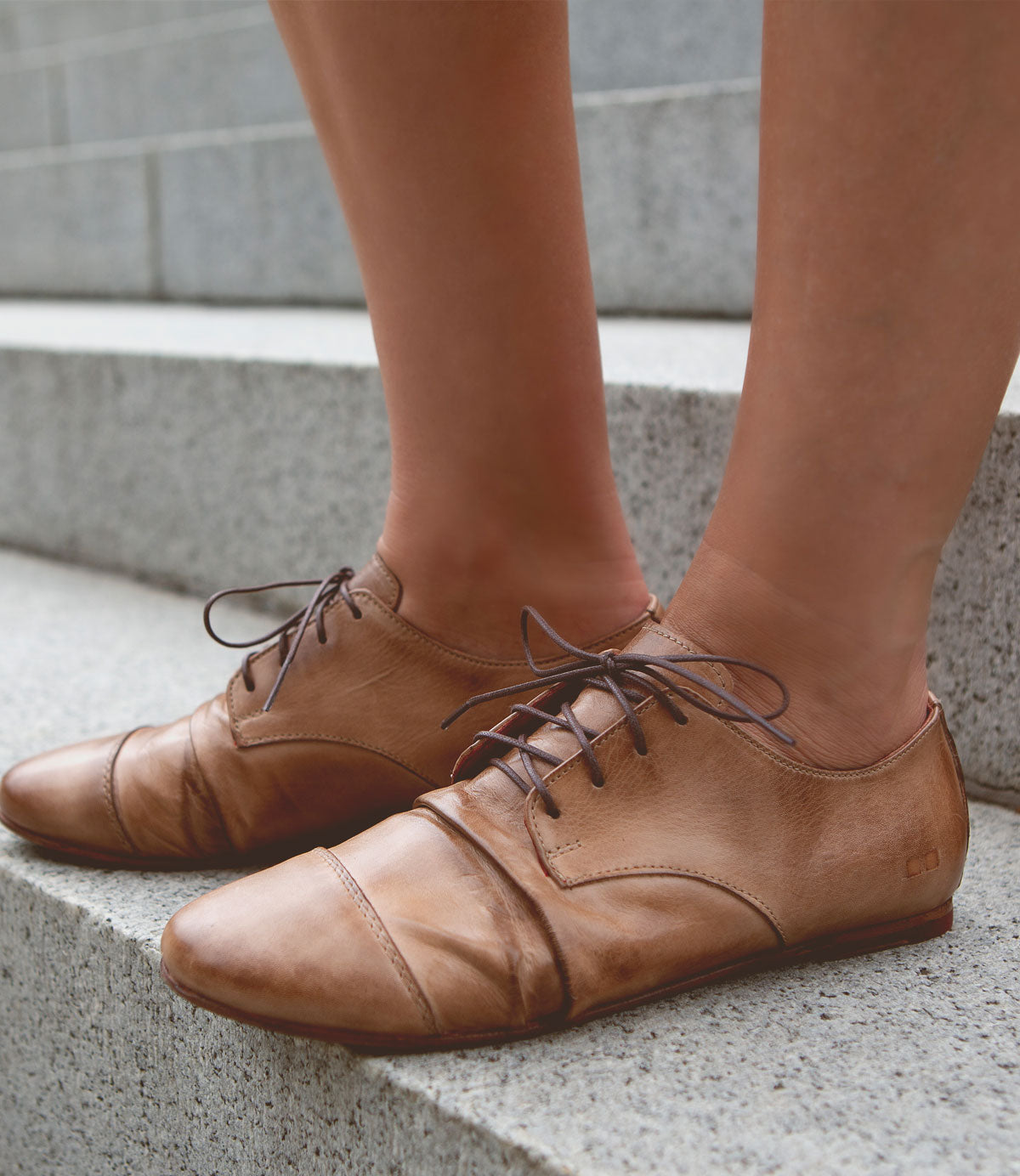 A person wearing the Bed|Stü Rumba II stylish comfort brown lace-up leather shoes stands on concrete steps.