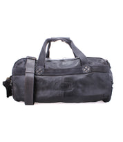 The Bed|Stü Ruslan is a black leather duffel bag featuring two handles, sturdy canvas straps, a detachable shoulder strap, and a front zipper pocket. The brand logo appears on the front, making it the ideal travel companion for any adventure.