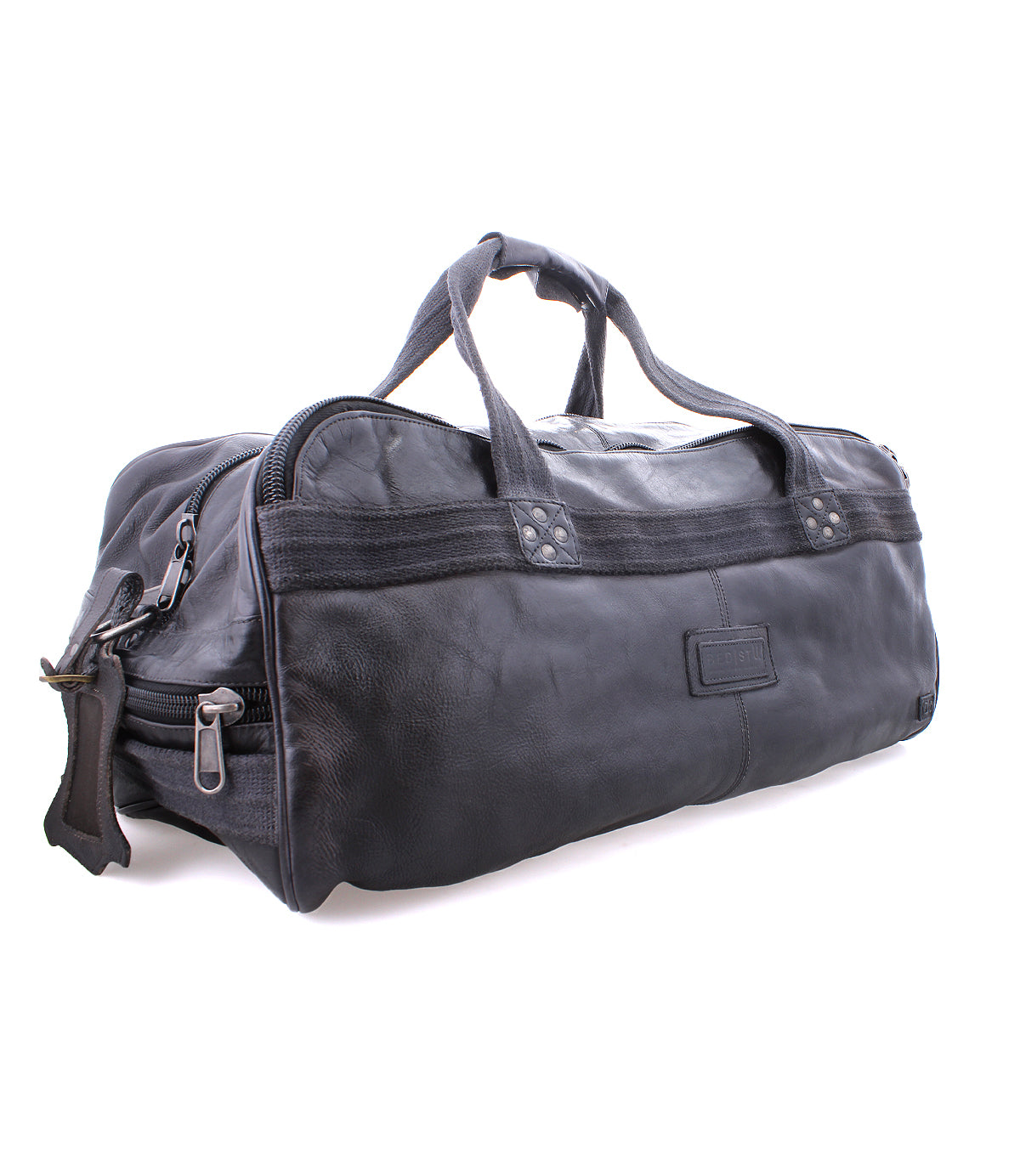 The Bed|Stü Ruslan is a black leather duffle travel bag featuring two handles, sturdy canvas straps, secure zipper closures, and a rectangular patch on the side, shown against a white background.