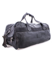 The Bed|Stü Ruslan is a black leather duffle travel bag featuring two handles, sturdy canvas straps, secure zipper closures, and a rectangular patch on the side, shown against a white background.