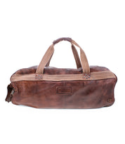 The Bed|Stü Ruslan is a brown leather duffel bag featuring durable beige canvas straps, a zipper closure, and a small front pocket. This leather travel duffel is shown on a white background.