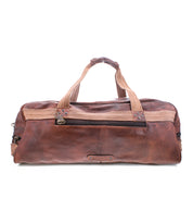 The Bed|Stü Ruslan is a brown leather duffel bag with durable canvas straps and tan fabric handles, featuring a front zipper pocket—an ideal travel bag displayed against a white background.