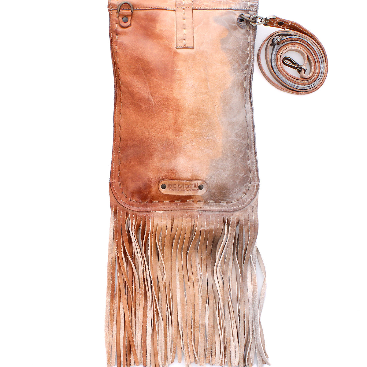 The Sandy Lane II by Bed|Stü is a handmade brown vegetable-tanned leather crossbody bag, featuring long fringe, metal studs, and an adjustable strap coiled beside it, displayed against a white background.