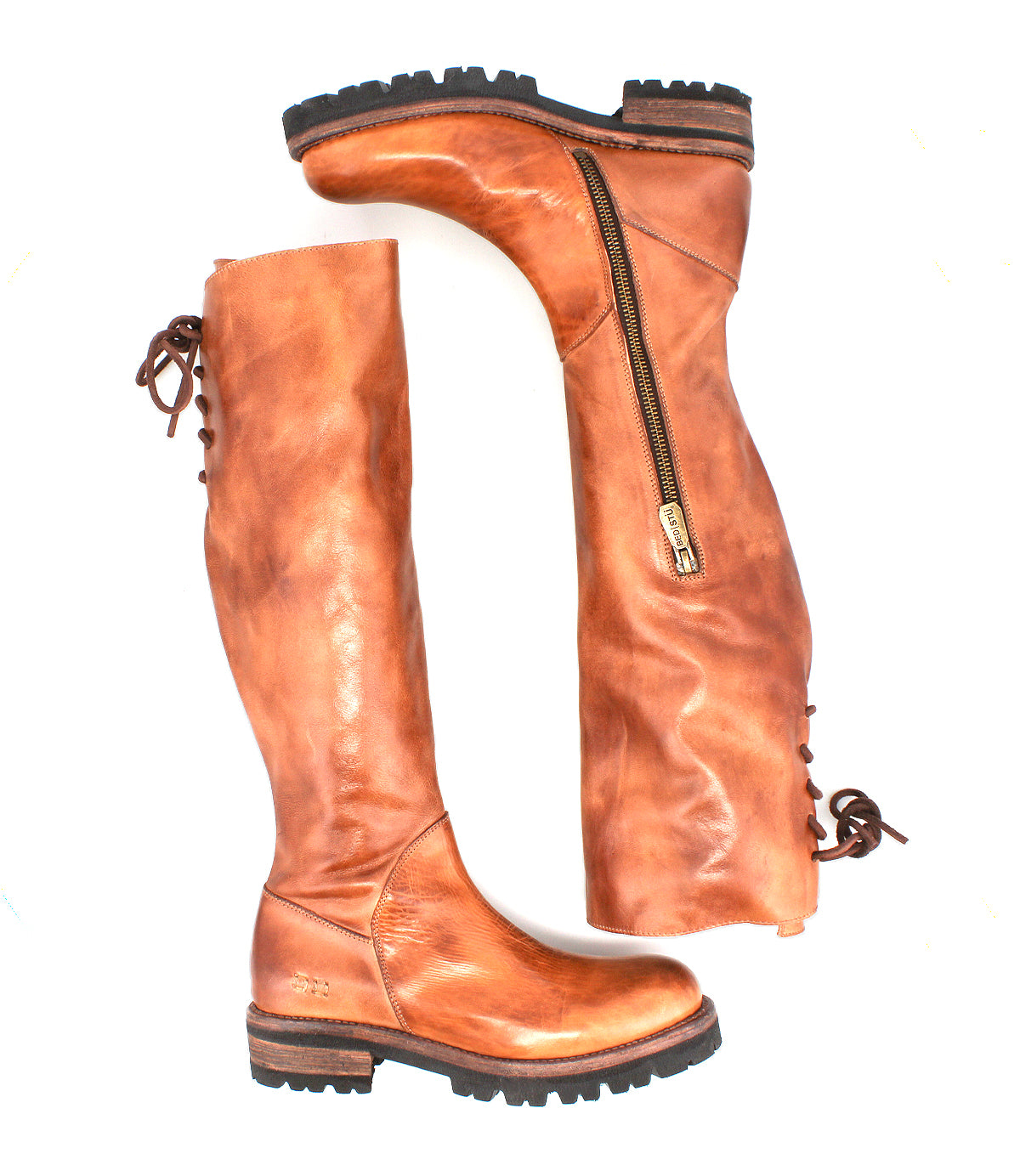 Introducing the Scope boots by Bed|Stü—a pair of tall boots expertly crafted from supple, vegetable-tanned leather, featuring convenient side zippers and distinctive lace-up backs. Shown on a white background, one boot stands upright while the other lies flat to highlight their unique design details.