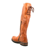 The Scope boot by Bed|Stü is a tall style crafted from vegetable-tanned leather, showcasing a distinctive lace-up back detail, convenient side zipper, and a chunky black-brown sole. Pictured from an angle against a white background.