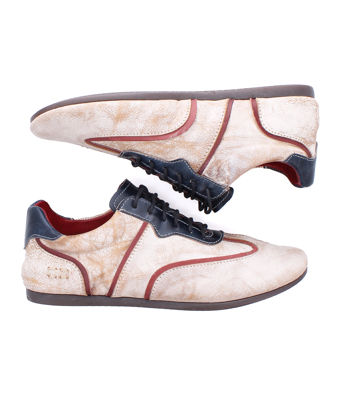 The Bed|Stü Scurry II sneakers are crafted from beige leather and feature dark brown soles, black laces, and contrasting dark and red trim. With a low-profile silhouette and lace-up design, they are shown in a side profile view against a white background.