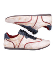 The Bed|Stü Scurry II sneakers are crafted from beige leather and feature dark brown soles, black laces, and contrasting dark and red trim. With a low-profile silhouette and lace-up design, they are shown in a side profile view against a white background.