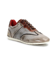 The Scurry sneaker by Bed|Stü is a gray and brown retro-inspired shoe made from vegetable-tanned leather, featuring black stitching, a lace-up front, red inner lining, and a white rubber sole for everyday durability. The shoe is positioned at an angle on a white background.