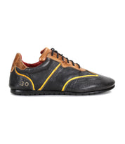 The Bed|Stü Scurry is a black and brown retro-inspired sneaker made from vegetable-tanned leather with yellow accents, featuring a low-profile design, durable rubber sole, and lace-up closure—shown in a left side profile view on a white background.