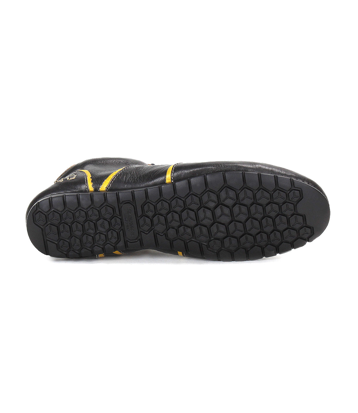 The image displays the bottom view of Bed|Stü's Scurry sneaker—a black, retro-inspired shoe featuring a hexagonal tread pattern and yellow accents, crafted for everyday durability.