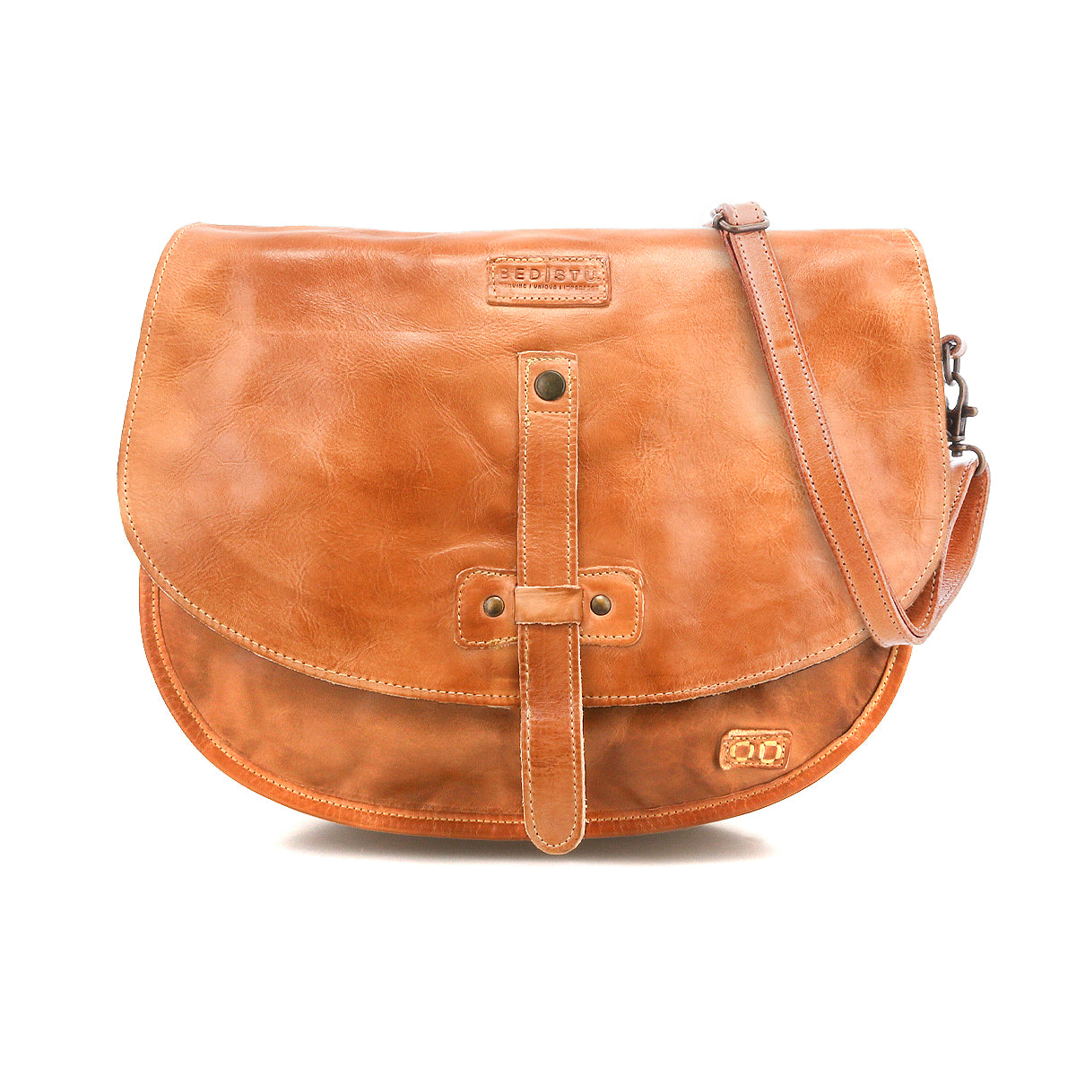 The Bed|Stü Sequoia is a brown vegetable-tanned leather crossbody satchel featuring a front flap, buckle strap closure, and an adjustable shoulder strap, displayed against a white background.