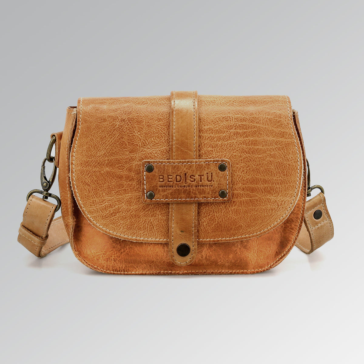 Light brown Studio Shoreline II Body crossbody bag by Bed|Stü, featuring a front flap, metal hardware, and a signature "Bed|Stü" logo patch on the front, offering a distinctive design that stands out against a plain gray background.