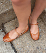 A person wearing the Bed|Stü Shuffle III brown leather Mary Jane shoes, crafted from supple leather, stands on concrete steps.