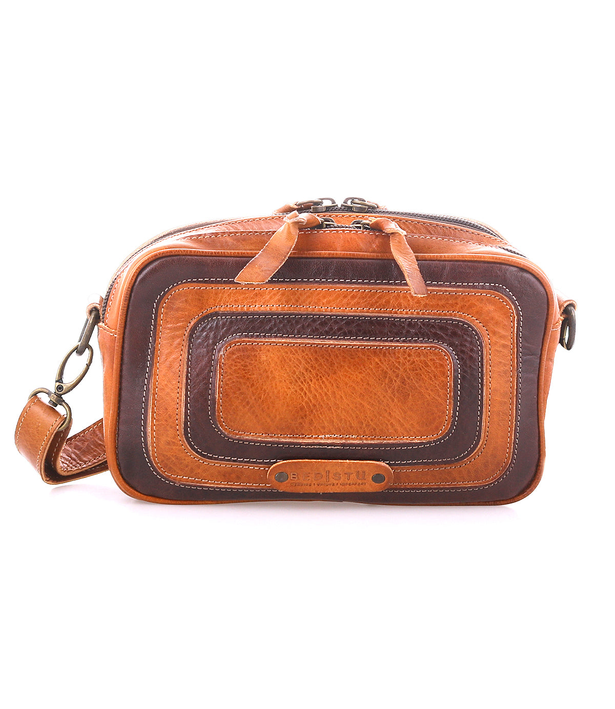 The Bed|Stü Shy compact leather bag in brown and dark brown features zippered compartments, an adjustable strap, dual pockets, and decorative stitching, displayed against a white background.
