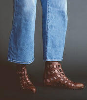 A person wearing light blue jeans and Skyline brown ankle boots by Bed|Stü, handcrafted in Italy, stands against a dark background.